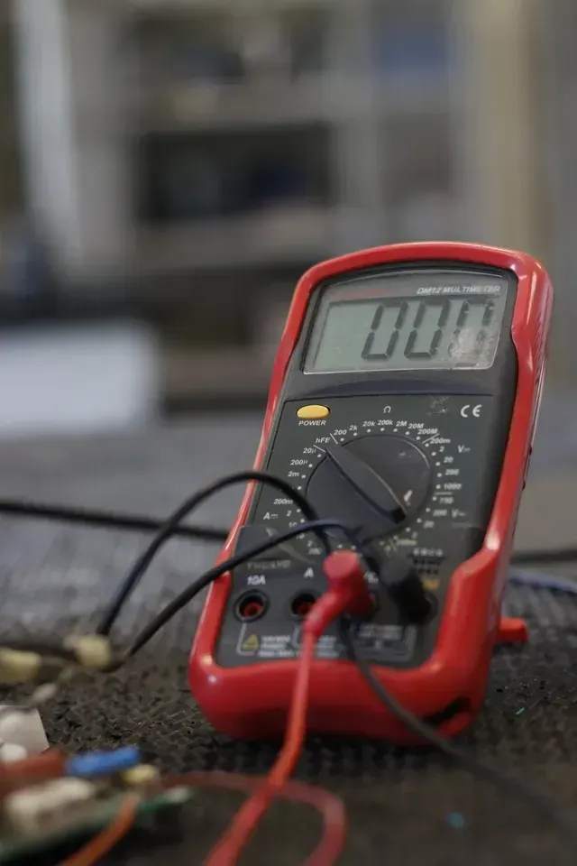 A red digital multimeter displays a reading of 0.00