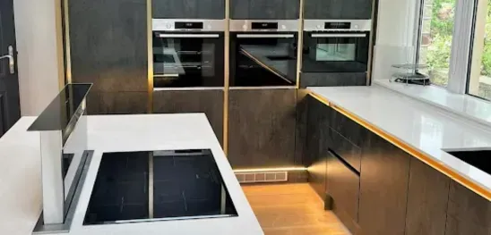 A kitchen with a sink , stove , ovens and a window.