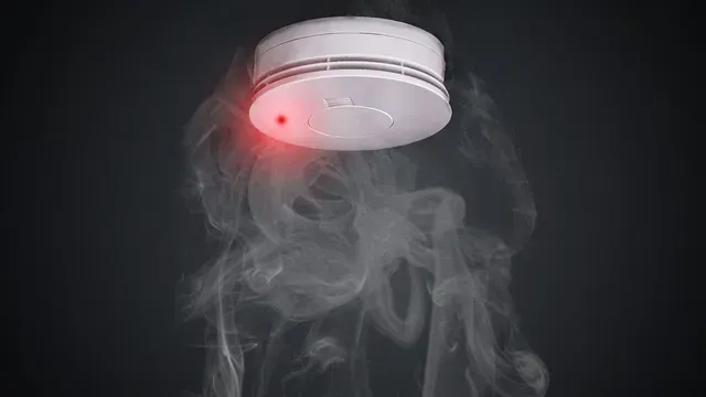 A smoke detector with smoke coming out of it and a red light on it.