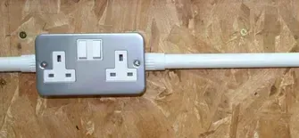 A close up of a electrical outlet on a wooden wall.
