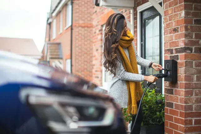 A woman is charging her electric car outside of her house.