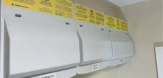 A row of white cabinets with yellow labels on them are hanging on a wall.
