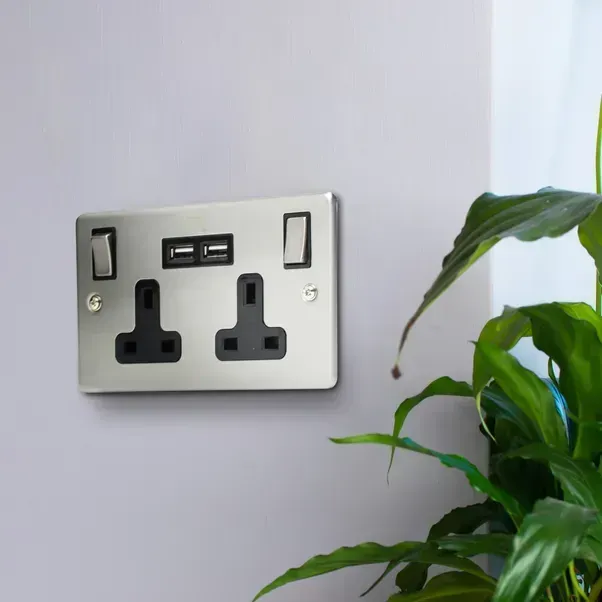 A stainless steel electrical outlet on a wall next to a plant